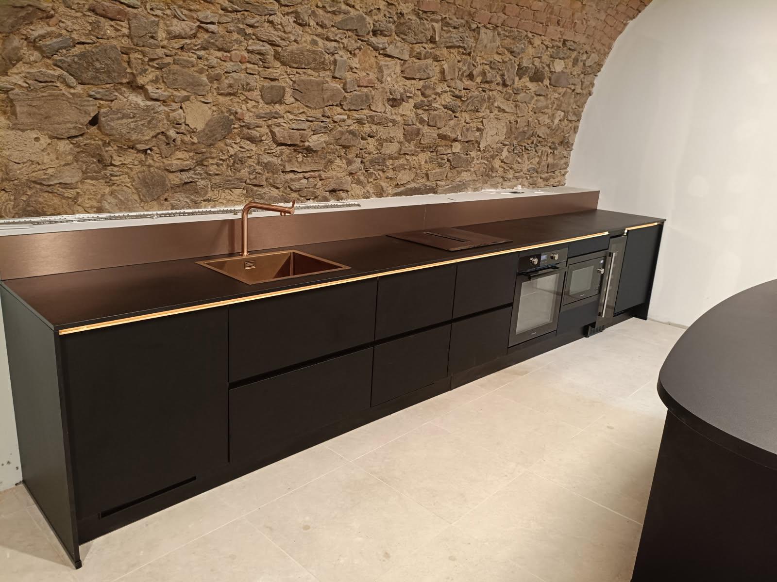 Cuisine noire avec plan cuivré et mur en pierre
